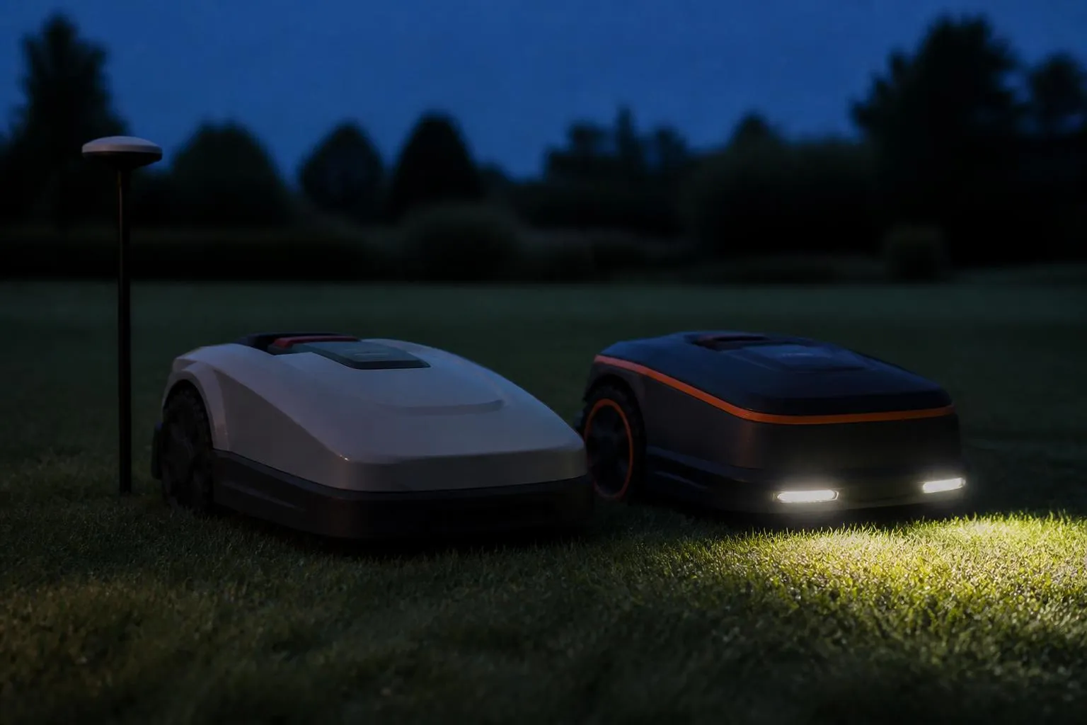 Deux robots tondeuses arrêtés côte à côte sur une pelouse au crépuscule, l'un projetant le faisceau de ses phares devant lui